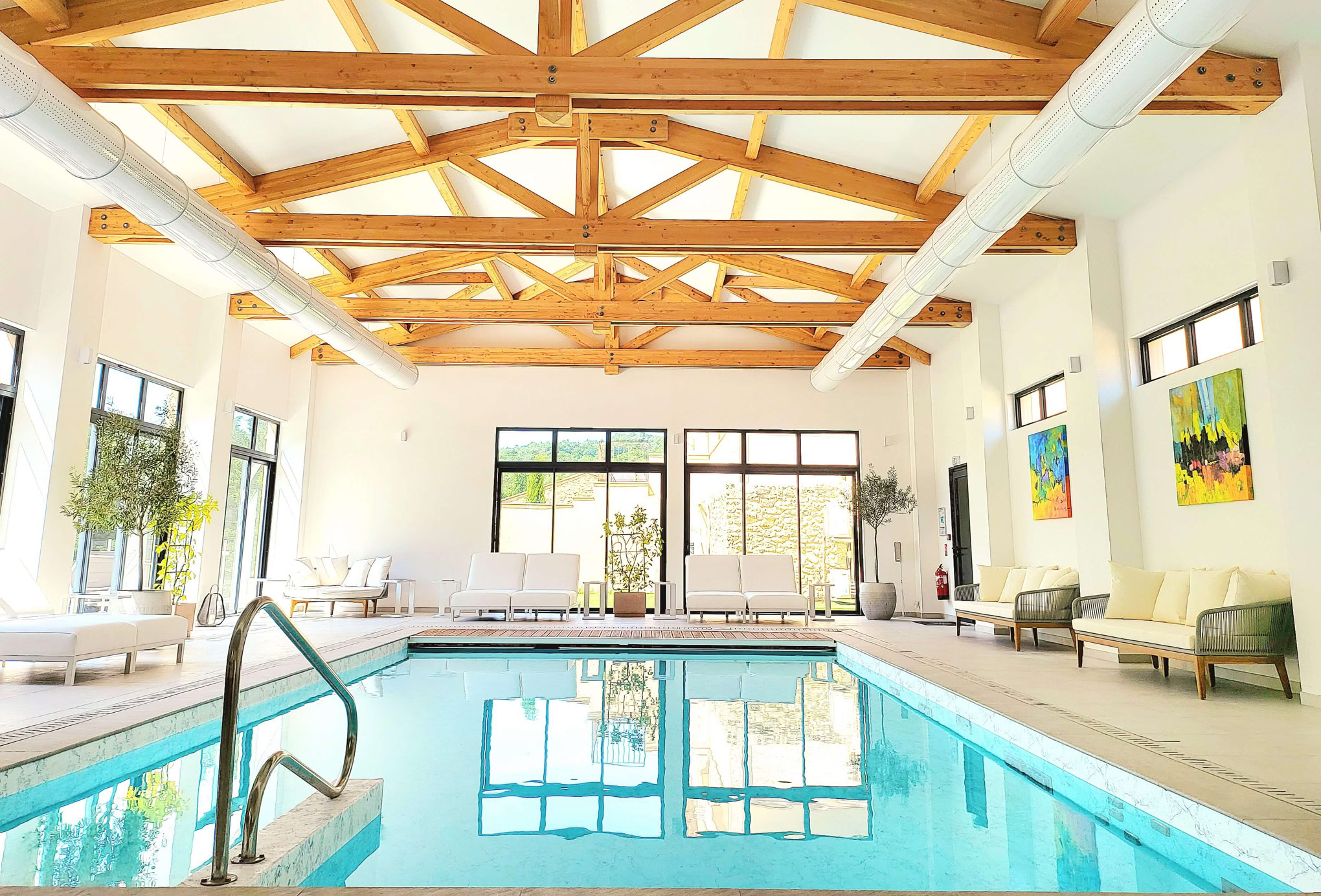 Piscine intérieure avec plafond en bois, grandes fenêtres, et chaises longues autour.